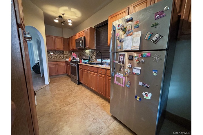 Kitchen with appliances with stainless steel finishes, decorative backsplash, light countertops, arched walkways, and brown cabinetry