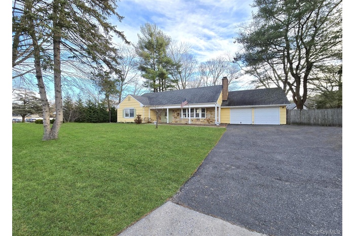 Ranch-style home featuring covered porch, a chimney, driveway, an attached garage, and roof with shingles
