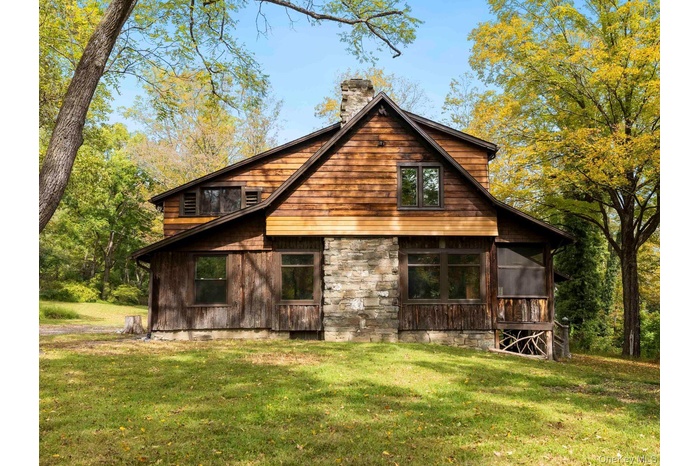 Rear view of property featuring a sunroom, a chimney, a yard, and stone siding