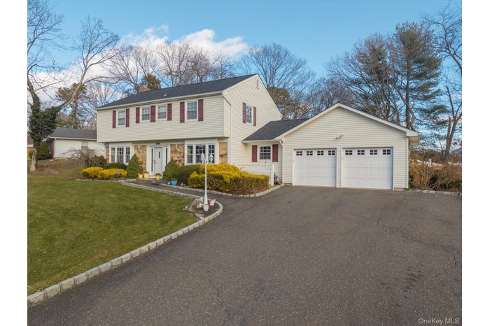 Colonial home featuring a front lawn, driveway, an attached garage, and roof with shingles