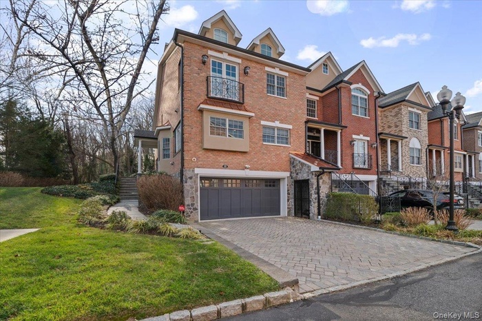 View of front of home with decorative driveway, brick siding, an attached garage, a front yard, and stone siding