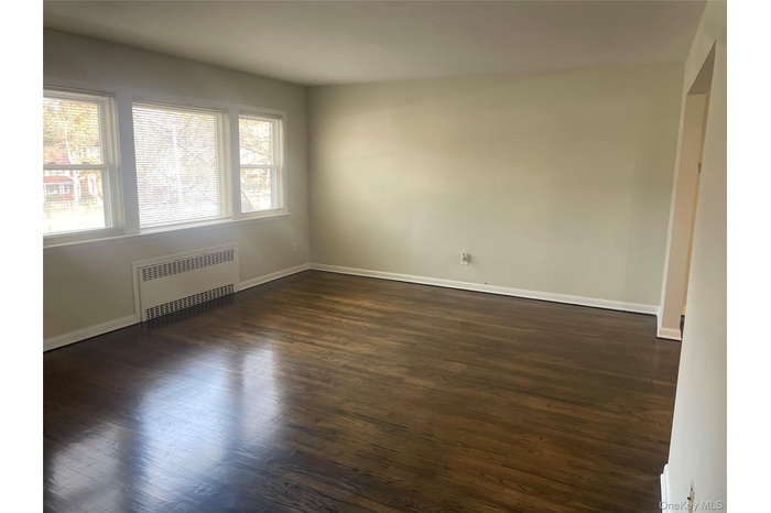 Empty room with dark wood-style flooring and radiator heating unit