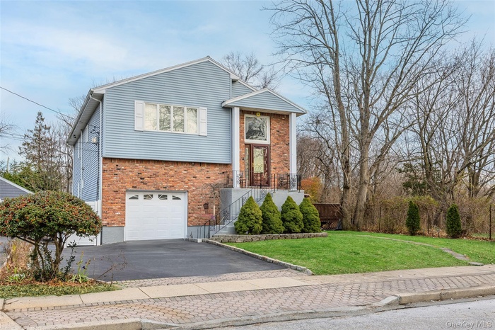 View of front of property featuring a front lawn, driveway, brick siding, a garage, and stairs