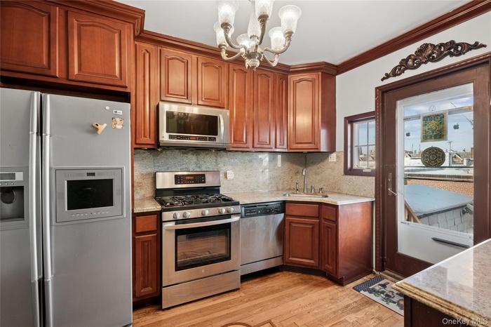 Kitchen with appliances with stainless steel finishes, a chandelier, light stone counters, light wood-style floors, and hanging light fixtures