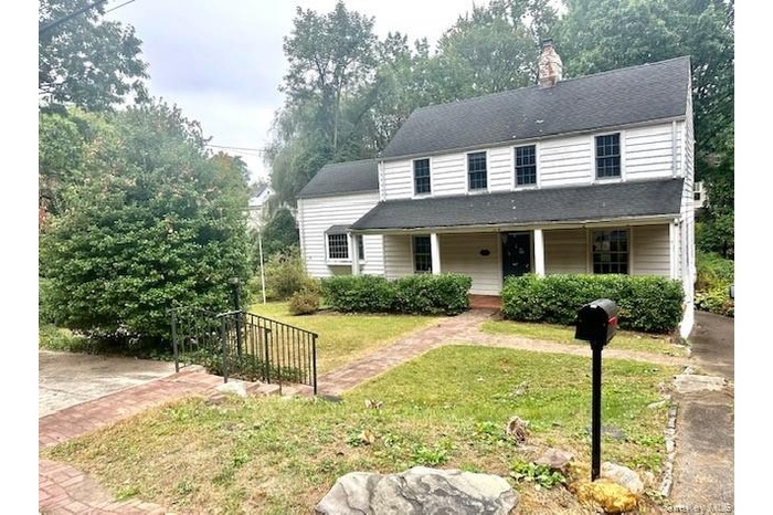 View of front of house with a porch, a front lawn, a chimney, and view of wooded area