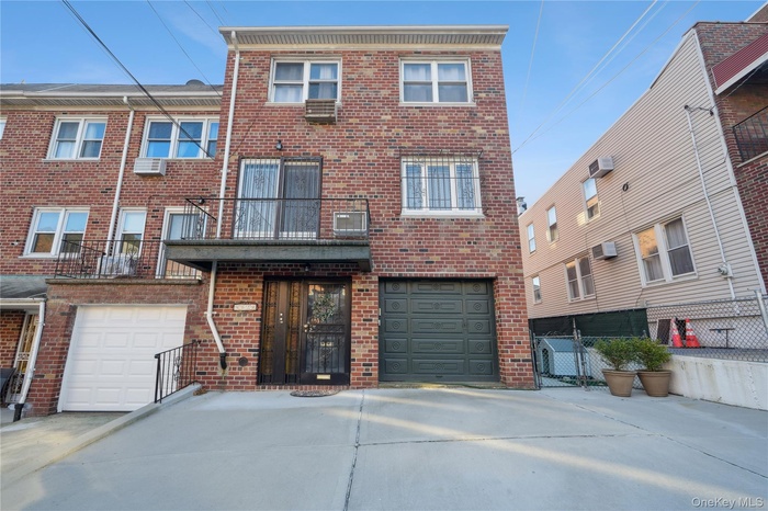 View of front of house featuring a balcony, brick siding, driveway, and an attached garage