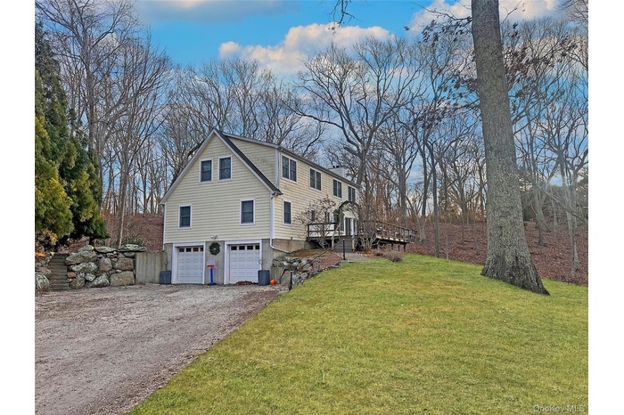 View of property exterior featuring a yard, an attached garage, a wooden deck, driveway, and a chimney