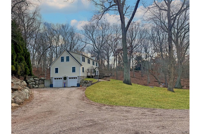 View of side of property featuring a lawn, driveway, a garage, a chimney, and view of scattered trees