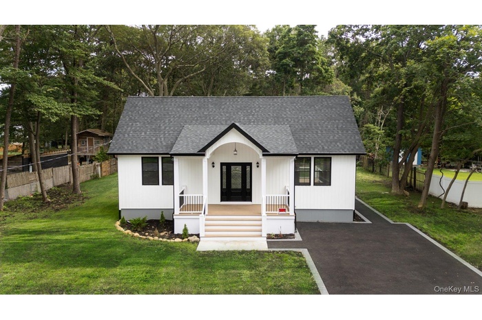 View of front facade with roof with shingles, a porch, and view of wooded area