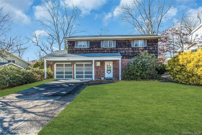 View of front of property with asphalt driveway, a front yard, a shingled roof, a garage, and brick siding