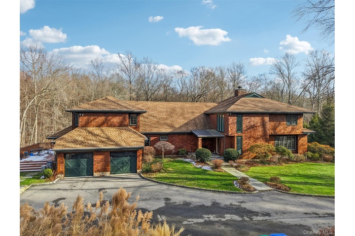 View of front of property with asphalt driveway, a chimney, a front yard, a garage, and a shingled roof