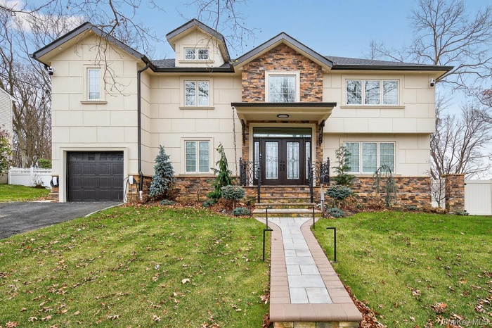 View of front of property with stone siding, an attached garage, asphalt driveway, french doors, and a shingled roof