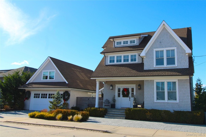 Shingle-style home featuring a porch, a shingled roof, a garage, and driveway