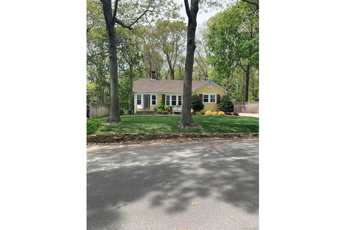Ranch-style home with a chimney and view of wooded area