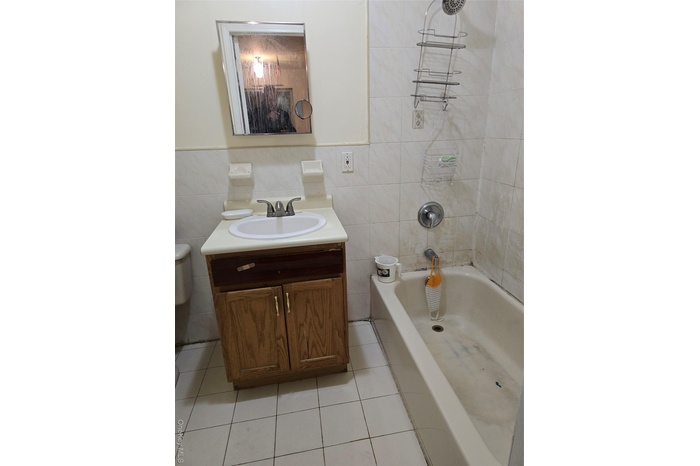Bathroom with tile walls, vanity, light tile patterned floors, and shower / bath combination