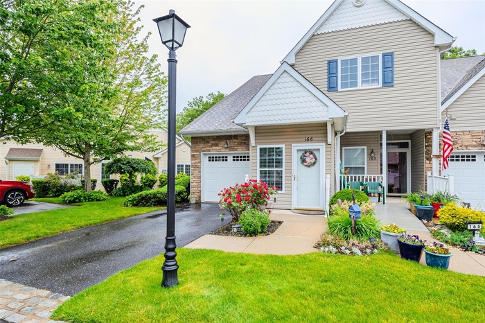 View of front facade featuring asphalt driveway, an attached garage, a front yard, covered porch, and stone siding