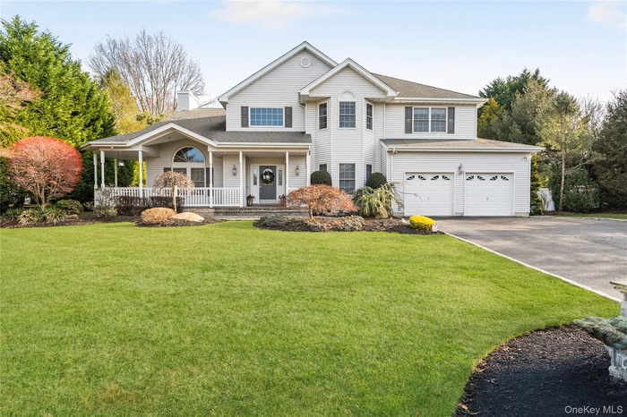 View of front of property with a porch, asphalt driveway, a front lawn, a garage, and a shingled roof