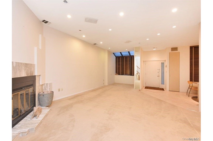 Unfurnished living room with a glass covered fireplace, recessed lighting, light carpet, and stairway