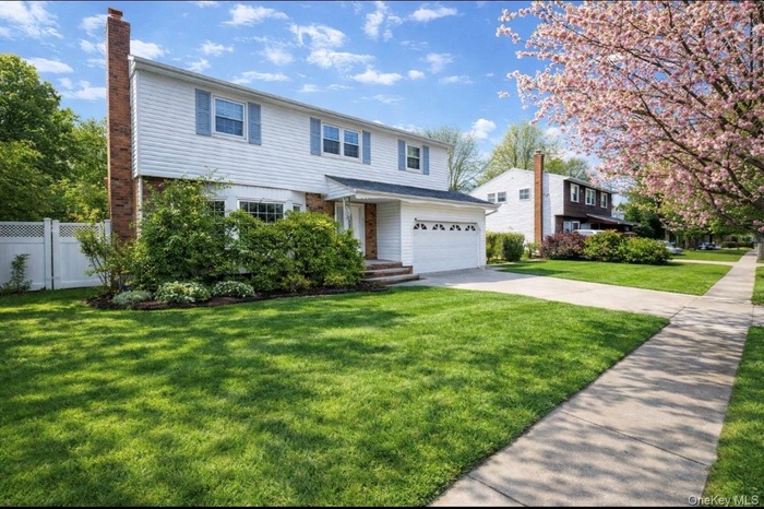 View of front facade featuring concrete driveway, a chimney, brick siding, and an attached garage