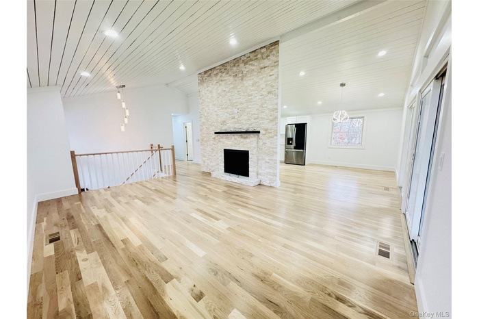 Unfurnished living room featuring light wood finished floors, a stone fireplace, vaulted ceiling, and wood ceiling