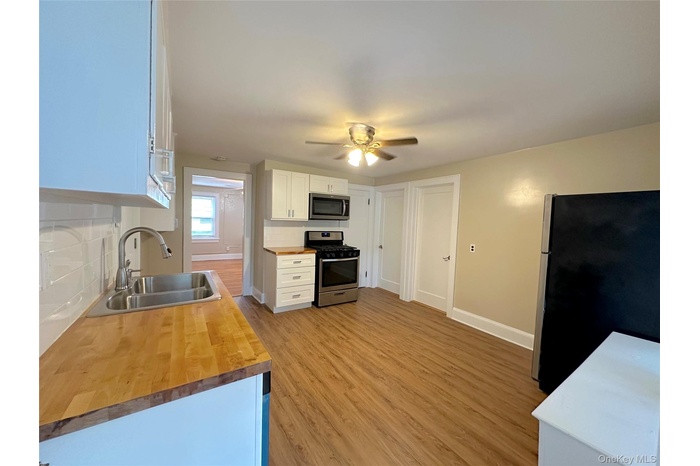 Kitchen with white cabinetry, butcher block counters, appliances with stainless steel finishes, decorative backsplash, and light wood-style flooring