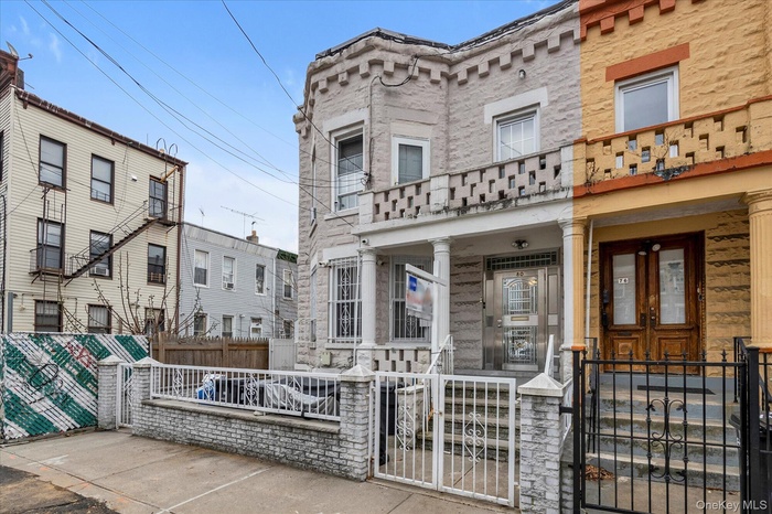 View of front of home with a fenced front yard, a gate, stone siding, and a balcony