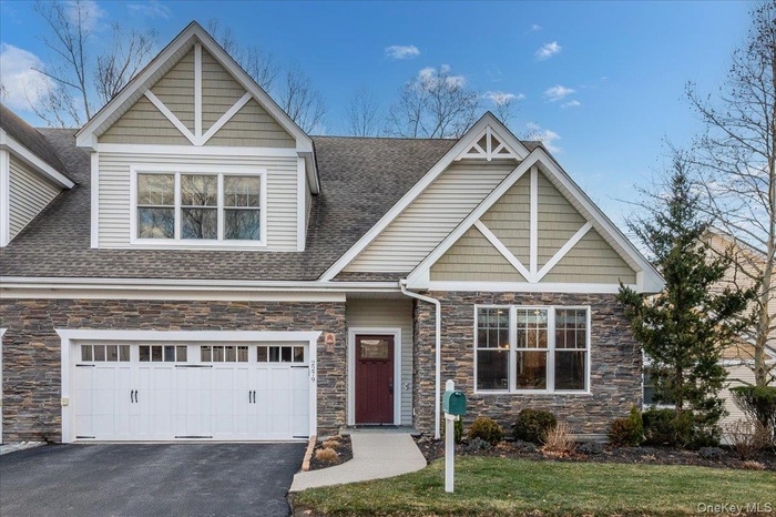Craftsman-style home featuring stone siding, driveway, a garage, a front yard, and roof with shingles