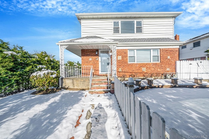 View of front of house featuring brick siding, a porch, and roof with shingles