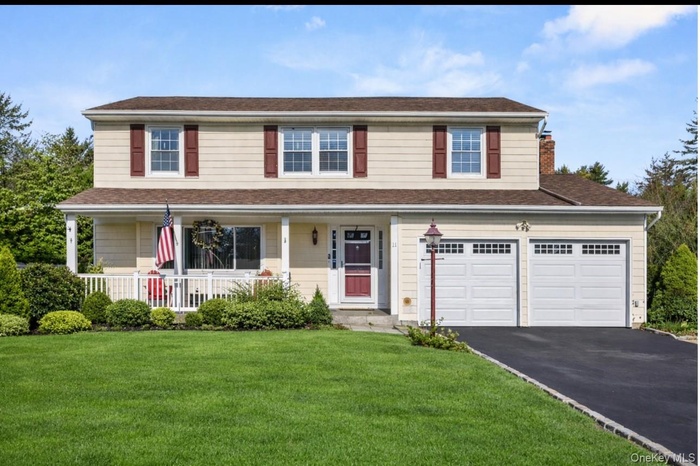 View of front of property featuring a porch, a front yard, asphalt driveway, a garage, and a chimney