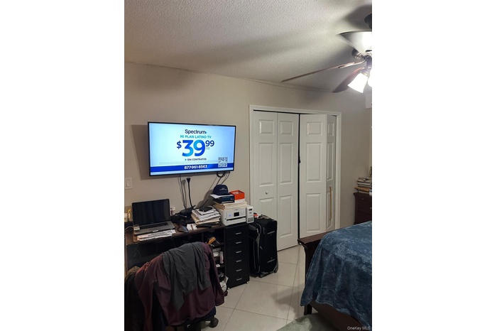 Bedroom with light tile patterned floors, a textured ceiling, a closet, and a ceiling fan