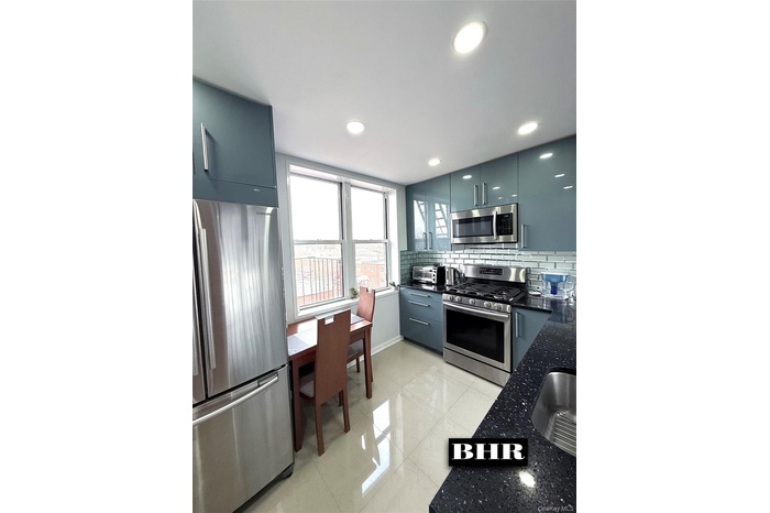 Kitchen featuring stainless steel appliances, modern cabinets, decorative backsplash, dark stone counters, and light tile patterned flooring