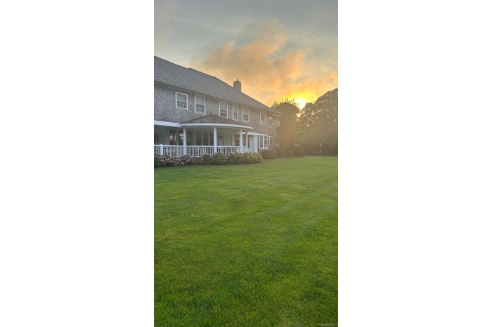 Back of property at dusk featuring a lawn, a chimney, and a porch