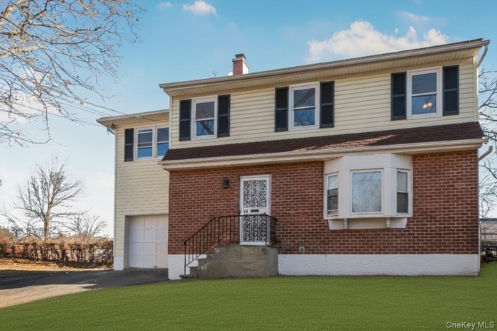 View of front of home featuring driveway, a chimney, an attached garage, and a front lawn