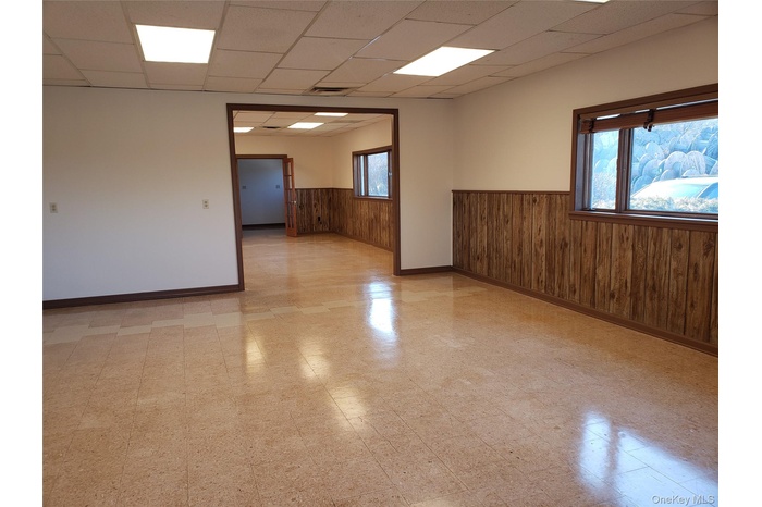 Empty room with light flooring, wood walls, a drop ceiling, and wainscoting