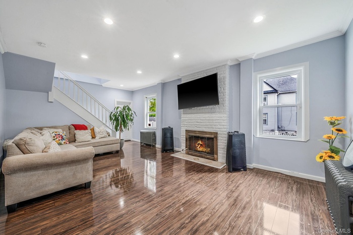 Living area with ornamental molding, stairs, wood finished floors, a brick fireplace, and radiator heating unit