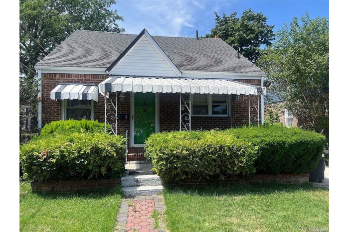 Bungalow-style house with brick siding, roof with shingles, a front yard, and covered porch