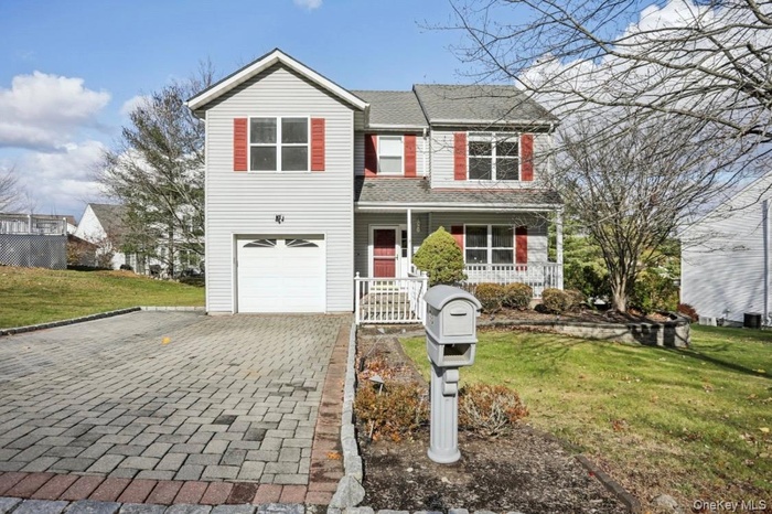 Traditional home with covered porch, a front yard, decorative driveway, and a shingled roof