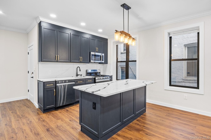 Kitchen featuring light stone counters, hanging light fixtures, stainless steel appliances, ornamental molding, and dark wood-type flooring