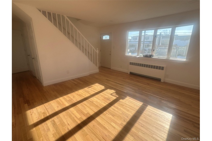 Unfurnished living room featuring light wood finished floors, radiator heating unit, and stairs