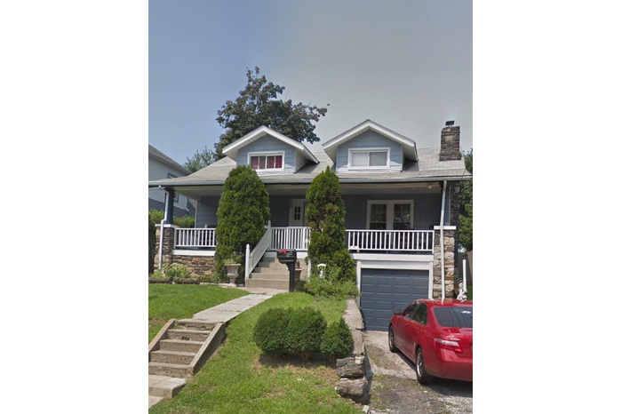 Bungalow-style home with a porch, a chimney, driveway, a garage, and stone siding