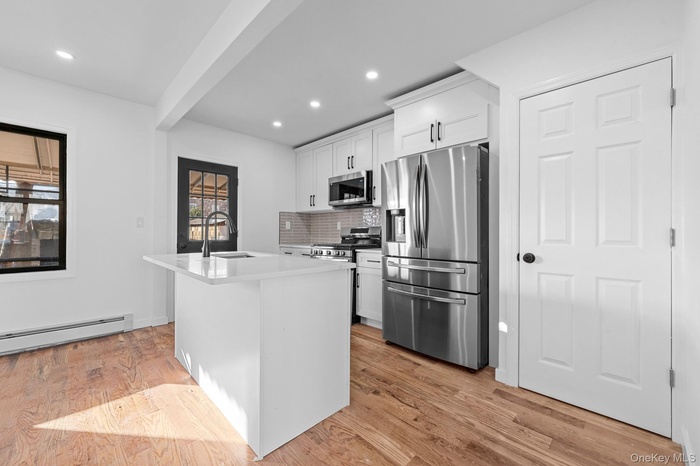 Kitchen with stainless steel appliances, a center island with sink, white cabinets, light wood-style flooring, and backsplash