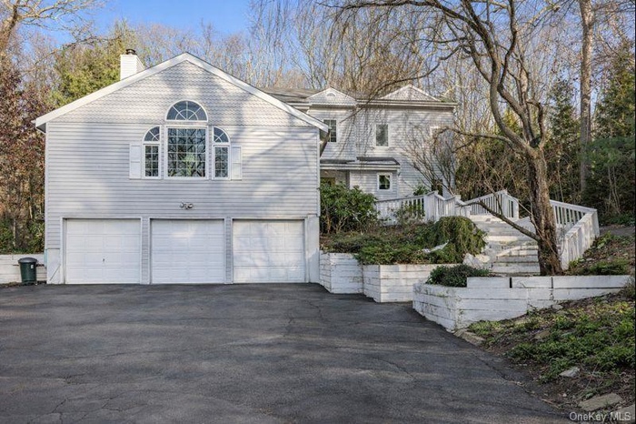 View of property exterior featuring asphalt driveway, a chimney, a garage, and stairway