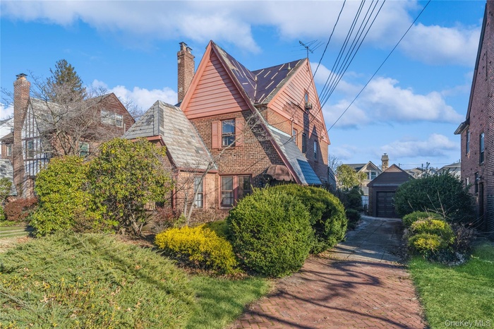 View of side of property with brick siding, an outdoor structure, a chimney, and a high end roof