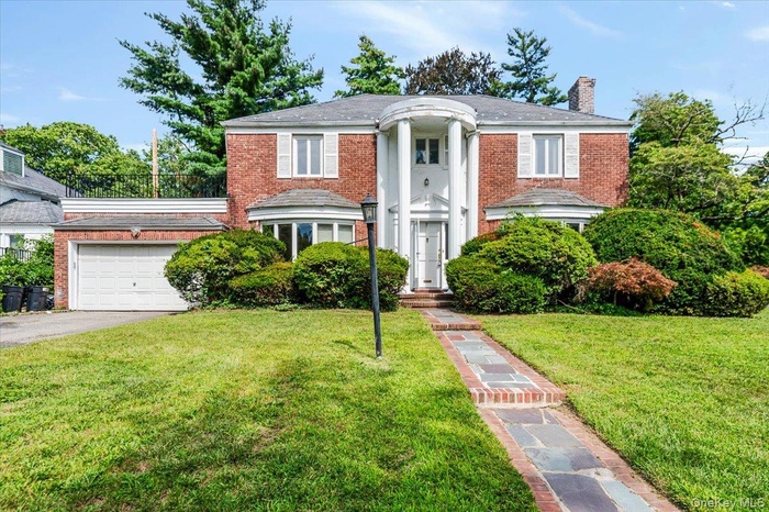Neoclassical home with brick siding, a chimney, a front yard, and an attached garage