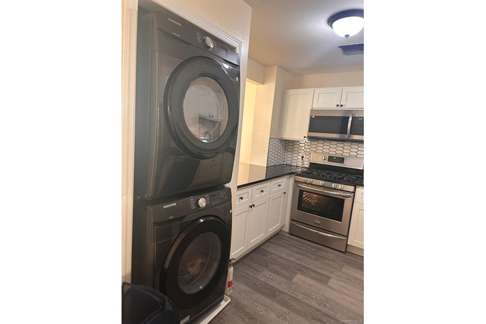 Laundry room featuring stacked washing machine and dryer and dark wood-type flooring
