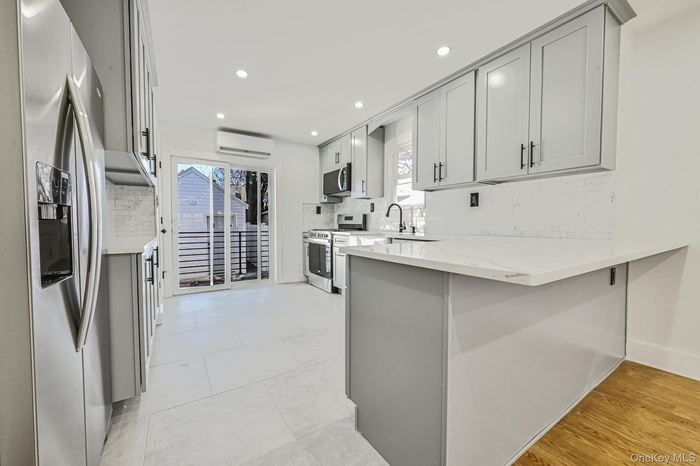 Kitchen featuring stainless steel appliances, a peninsula, light stone counters, tasteful backsplash, and gray cabinets
