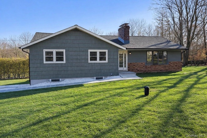 Rear view of house featuring a lawn, a chimney, and brick siding