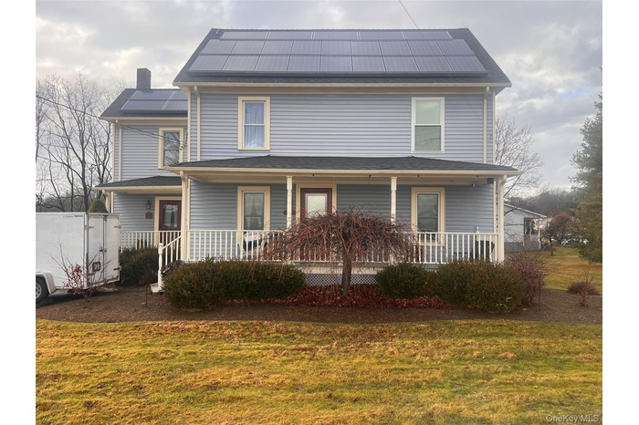 View of front of house featuring solar panels, a porch, a front yard, and a chimney