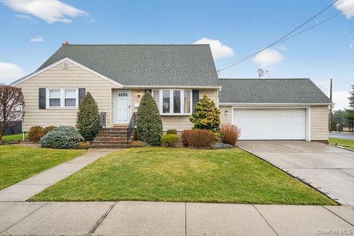View of front facade with a garage, a front yard, driveway, and roof with shingles