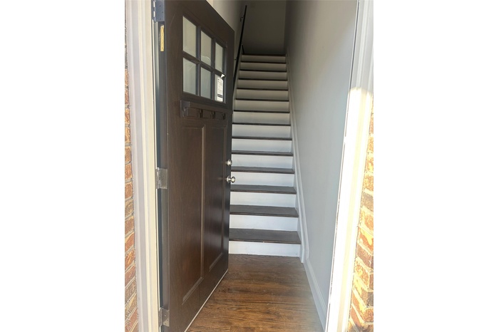 Staircase featuring wood finished floors and brick wall